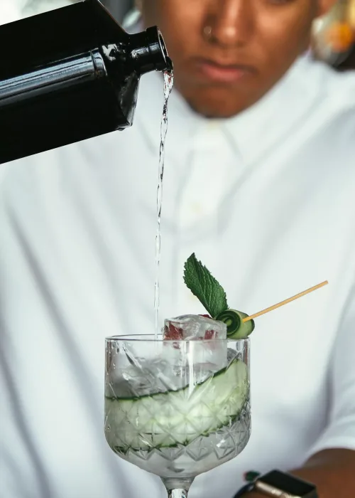 Detail of alcohol poured in a cocktail glass by a mixed race male expert bartender at the bar counter